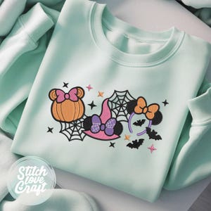 Può includere: Una felpa girocollo color verde menta con un ricamo raffigurante una zucca con fiocco rosa, un cappello da strega con fiocco viola, una ragnatela, un cerchietto con orecchie arancioni e pipistrelli neri, decorata con piccole stelle.