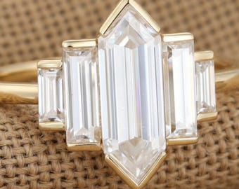 May include: A gold ring featuring a large, rectangular, clear gemstone with a pointed top and bottom, flanked by smaller rectangular stones. The ring has a simple, elegant design, perfect for a special occasion.