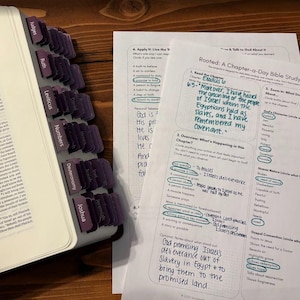 Może przedstawiać: Otwarta Biblia z fioletowymi zakładkami z nazwami ksiąg i notatkami do nauki na białym papierze. Notatki do nauki zawierają tekst "Rooted: A Chapter-a-Day Bible Study Template". Biblia jest otwarta na Księgę Wyjścia.