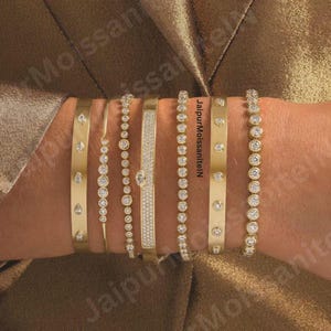 May include: Several gold bracelets, each with a unique design featuring diamonds. Styles include bezel-set stones, teardrop gems, and a pave band. The bracelets are shown on a wrist, highlighting the different textures and designs.