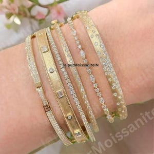 May include: A collection of gold bracelets with various designs, including diamond accents and textured surfaces. The bracelets are displayed on a wrist, showcasing the different styles and sparkle. The image includes the text "JaipurMoissaniteIN".