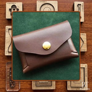 May include: A brown leather cardholder with a curved flap and a gold button closure. The cardholder is set against a green background, with wooden craft tools surrounding it. The leather appears smooth and well-crafted.