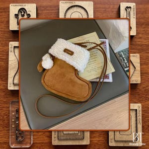 May include: A brown suede-like stocking-shaped purse with a fluffy white cuff and a small pom-pom. The purse has a long, thin brown strap. The word "CLEAROK" is visible on the cuff. The purse is on a neutral background.