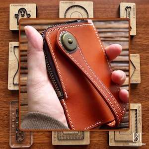 May include: A brown leather wallet with a zipper closure and a wrist strap. The wallet has white stitching and a metal button closure. The image also shows various wooden craft tools.