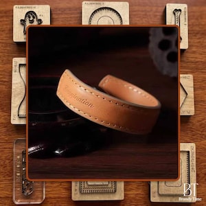 Puede incluir: Una pulsera de cuero marrón claro con la palabra "Imagination" grabada en la superficie. La pulsera está cosida con un hilo en contraste y está rodeada de herramientas de artesanía de madera.