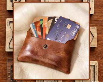 May include: A brown leather cardholder with a snap closure, filled with various credit cards. The cardholder sits on a white, fluffy surface. Wooden die-cut shapes surround the cardholder, adding a rustic touch. The cardholder is approximately 4 inches wide.