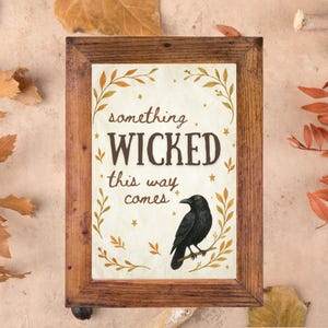 Può includere: Stampa incorniciata con la scritta "something WICKED this way comes" e un corvo nero posato su un ramo. La stampa ha uno sfondo color crema con accenti botanici dorati ed è incorniciata in una cornice di legno marrone rustico.