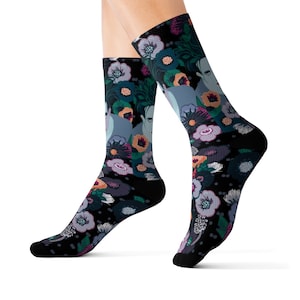 Puede incluir: Calcetines negros con un diseño floral en tonos azules, morados y naranjas. Los calcetines también tienen un diseño de rostro. Los calcetines se llevan en los pies de una persona.