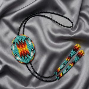 Peut inclure: Un bolo tie perlé avec un pendentif ovale turquoise orné d'un motif central rouge, jaune et orange. Le pendentif est entouré de perles blanches et noires. La cravate a un cordon en cuir noir et des embouts perlés.