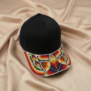 May include: A black baseball cap featuring a curved brim adorned with intricate, multi-colored beadwork in a geometric pattern. The beads are arranged in vibrant shades of red, orange, yellow, green, blue, and white, creating a star-like design.