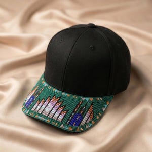 Könnte beinhalten: Eine schwarze Baseballkappe mit einem grünen Schirm, der mit aufwendigen Perlenarbeiten verziert ist. Das Perlenmuster zeigt geometrische Formen in Violett-, Blau-, Orange- und Weißtönen, die ein detailliertes Design auf der gesamten Schirmoberfläche bilden.