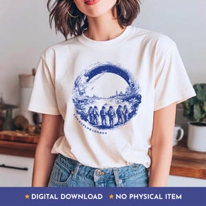 May include: Cream-colored t-shirt featuring a blue circular graphic with a landscape and figures, with the text "LOS EXPLORADORES". The shirt also has the text "DIGITAL DOWNLOAD" and "NO PHYSICAL ITEM".