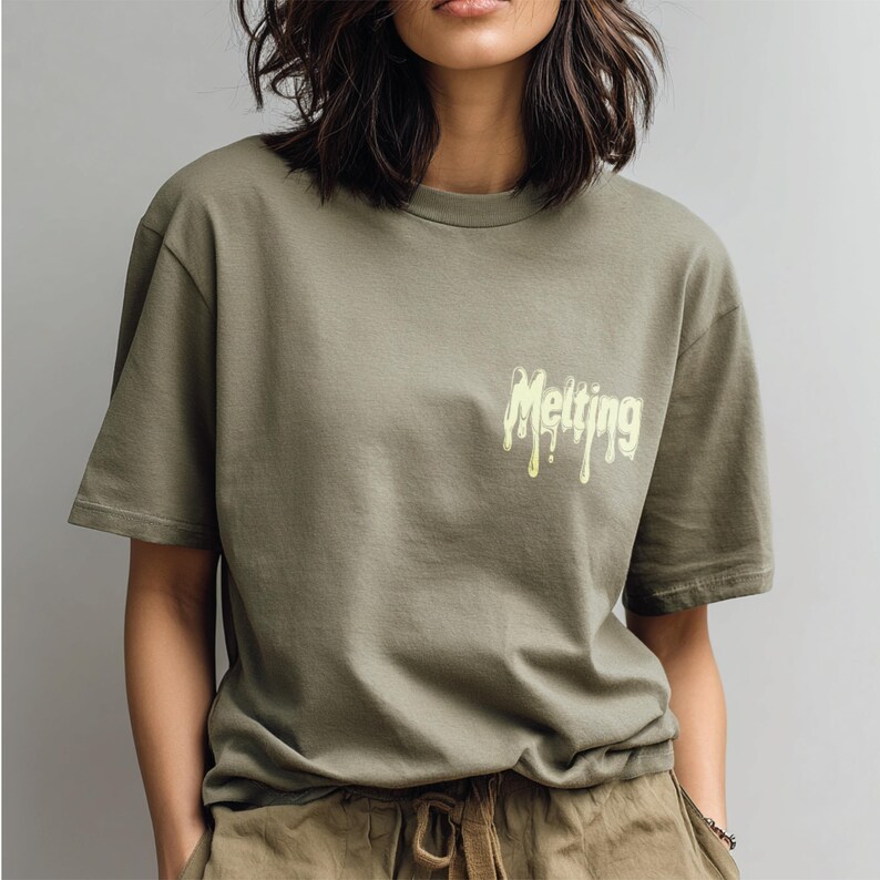May include: Olive green t-shirt with the word "Melting" in a dripping yellow font on the upper chest. The shirt has short sleeves and a relaxed fit. The model is wearing olive green pants.