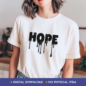 May include: A cream-coloured t-shirt featuring the word "HOPE" in large, black, dripping letters. The text has a distressed, textured effect. The t-shirt has short sleeves and a crew neck. The design is simple and striking.