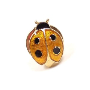Front view of the retro vintage ladybug tie tack. The metal is gold tone in color. The lady bug has an orange yellow enameled body and black enameled spots and head. The clutch on the back is round and is the type without a chain.