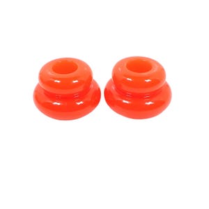 May include: Two vibrant orange candle holders. Each holder has a circular base, a rounded midsection, and a top with a circular opening. The glossy finish reflects light, creating a bright and cheerful appearance. The candle holders are set against a white background.