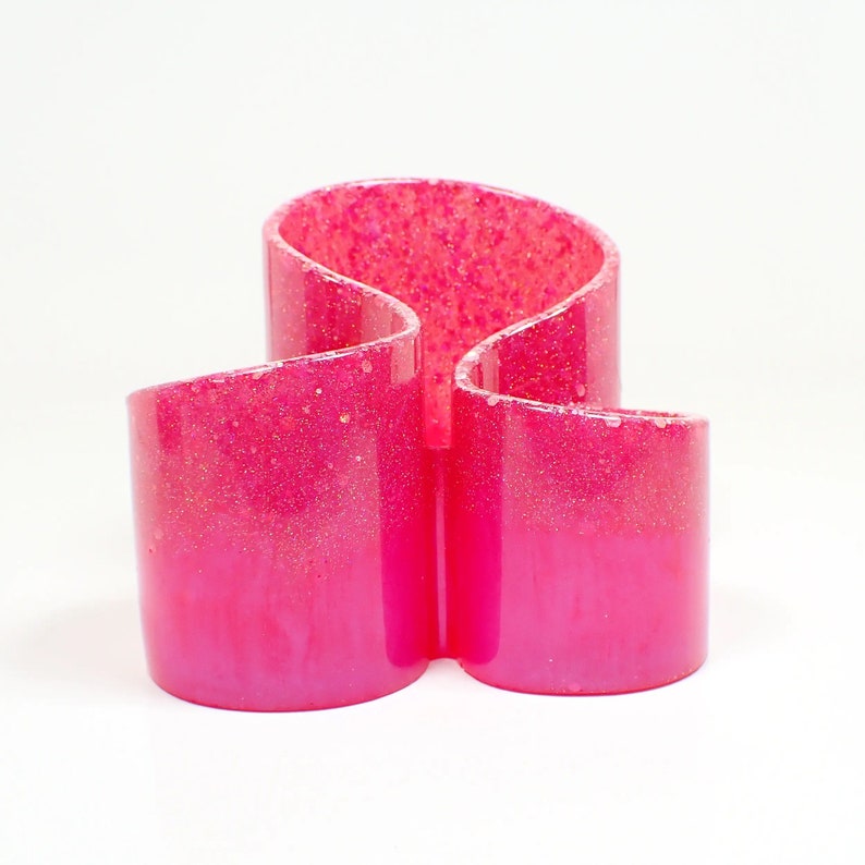 Front view of the handmade resin makeup brush holder. It has pink resin with iridescent glitter at the top. There are three round areas to hold the brushes with the back having the tallest side.