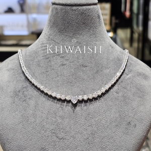 Puede incluir: Un collar de diamantes con un colgante en forma de corazón. El collar se exhibe en un maniquí gris. El nombre de la marca "KIIWAISH" está impreso en blanco en el maniquí.