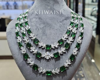 May include: Three-strand necklace with emerald green rectangular stones and white accents, displayed on a gray mannequin. The necklace has a layered design with the text "KIIWAISH" at the top.