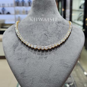 Op de afbeelding: Een goudkleurige ketting met een rij sprankelende, rond geslepen stenen. De ketting wordt gepresenteerd op een grijze mannequin. De merknaam "KIIWAISH" staat in het wit op de mannequin.
