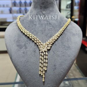 May include: A gold necklace with a floral pendant and teardrop-shaped dangles. The necklace is displayed on a grey mannequin. The brand name "KIIWAISH" is visible in white text.