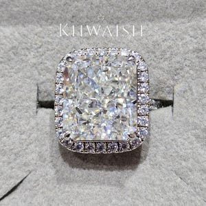 Peut inclure: Une bague en diamant de taille rectangulaire, entourée d'un halo de petits diamants. La pierre centrale est le point focal, avec une double rangée de gemmes. La bague est montée sur un anneau argenté, offrant un aspect luxueux.