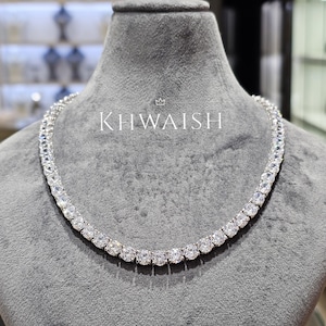 May include: A dazzling silver necklace featuring multiple round, clear gemstones. The necklace is presented on a grey mannequin. The word "KHWAISH" is printed in white on the mannequin.