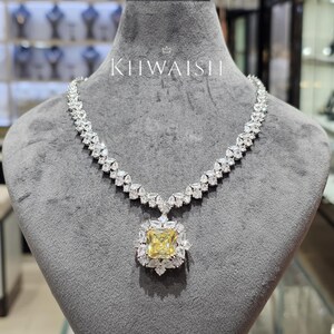 Puede incluir: Un collar con una piedra preciosa central amarilla de corte cuadrado rodeada por un halo de pequeñas piedras claras, unido a una cadena compuesta por múltiples piedras claras en forma de pera. El texto KHWAISH aparece sobre el collar.