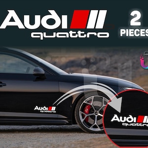 May include: Black car with white and red Audi Quattro decals. The decals are on the side of the car and on the wheel. The text "Audi Quattro" is displayed in white. The image also shows a close-up of the decal.