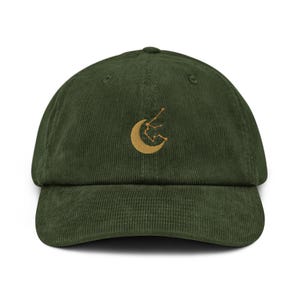 Könnte beinhalten: Grüne Cord-Baseballkappe mit gebogenem Schirm. Die Kappe hat ein goldfarbenes, gesticktes Design aus einem Mond und einer Sternenkonstellation. Klassischer, verstellbarer Stil.