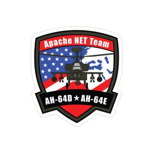 May include: A sticker featuring a black and gray Apache helicopter design. The sticker has a shield shape with the text "Apache NET Team" at the top and "AH-64D AH-64E" at the bottom. The background includes the American flag and a map.