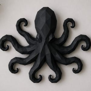 May include: A matte black wall sculpture of an octopus featuring a geometric, faceted design. The creature has a central head and eight radiating, curled tentacles, all constructed with sharp, angular planes that create a low-poly aesthetic.