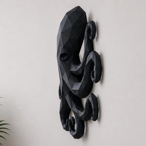 May include: A black wall-mounted octopus sculpture featuring a geometric, faceted design. The piece displays a multi-sided, angular surface structure that forms the head and multiple curled tentacles, creating a three-dimensional appearance.