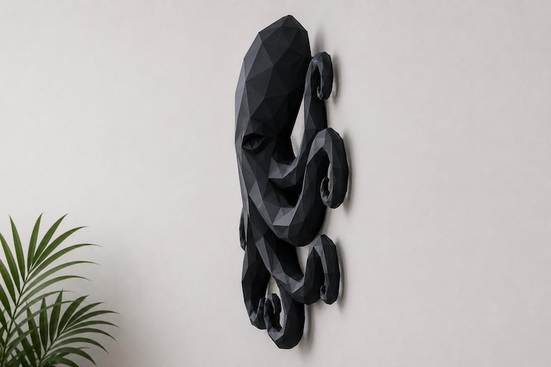 May include: A black wall-mounted octopus sculpture featuring a geometric, faceted design. The piece displays a multi-sided, angular surface structure that forms the head and multiple curled tentacles, creating a three-dimensional appearance.