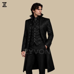Puede incluir: Un abrigo largo negro con cuello alto y chaleco a juego, ambos con un patrón de damasco tonal. El abrigo tiene una fila de botones en la parte delantera. Se lleva un corbatón negro con un alfiler decorativo central en el cuello, junto con pantalones negros.