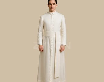 May include: A cream-colored, long-sleeved robe with a mandarin collar and a row of small buttons down the front. The robe features a matching belt and a long, vertical panel of fabric. The person is wearing black shoes.