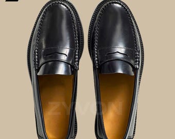 Op de afbeelding: Een paar zwarte leren penny loafers. De schoenen hebben een glanzende afwerking, een gestikte zool en een klassiek penny bandje detail. De binnenkant is lichtbruin.
