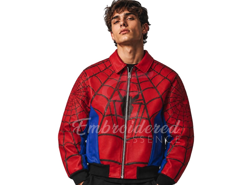 K&ouml;nnte beinhalten: Rote und blaue Jacke im Spider-Man-Design mit schwarzem Spinnennetz-Muster und schwarzem Spinnen-Emblem. Die Jacke hat einen Rei&szlig;verschluss, einen schwarzen Kragen und blaue Seitenteile. Der Text "Embroidered Essence" ist sichtbar.