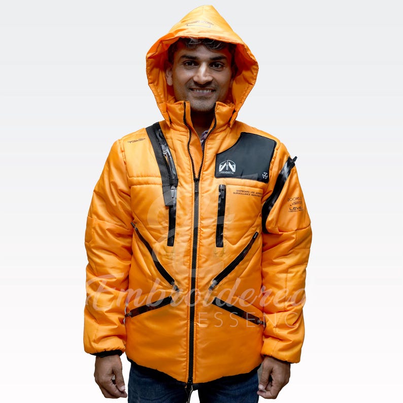May include: An orange hooded jacket with black accents and zippers. The jacket has a front zipper closure and multiple pockets. The text "Supreme of the Himalayas" is visible on the chest. The jacket is worn by a person.