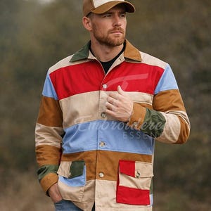 May include: A multi-colored patchwork jacket with a brown, red, blue, and tan color scheme. The jacket has a button-up front, two front pockets, and a green collar. A brown and tan baseball cap is worn.
