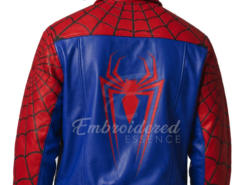 K&ouml;nnte beinhalten: Blaue und rote Lederjacke mit gro&szlig;em rotem Spinnenemblem auf dem R&uuml;cken. Die Jacke hat rote Spinnennetzdetails an den &Auml;rmeln und Schultern. Der Text "Embroidered Essence" ist auf der R&uuml;ckseite aufgedruckt.