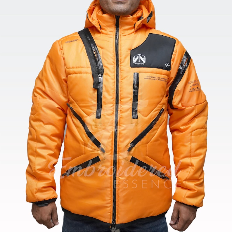 May include: Bright orange winter jacket with a hood and black accents. Features multiple zippered pockets and a quilted design. The jacket has text and logos on the chest and sleeves. The jacket is made of a durable, weather-resistant material.