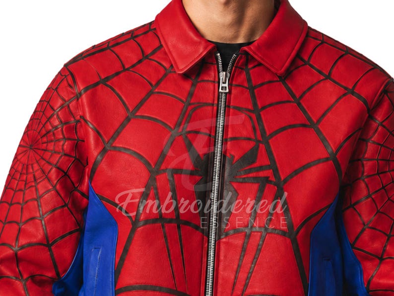 K&ouml;nnte beinhalten: Rote Lederjacke mit schwarzem Spinnennetz-Design und gro&szlig;em Spinnen-Emblem auf der Brust. Die Jacke hat einen Rei&szlig;verschluss und blaue Seitenteile. Der Text "Embroidered Essence" ist sichtbar.