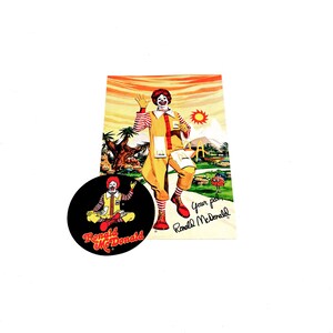 May include: A vintage McDonald's sticker featuring Ronald McDonald in a yellow and red costume. The sticker is round and has a black background with the words "Ronald McDonald" in red and white text. The sticker is perfect for collectors of vintage McDonald's memorabilia.