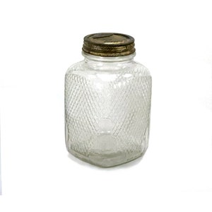 May include: A clear glass jar with a textured diamond pattern and a brass lid. The jar is empty.