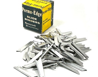 May include: A box of 200 silver Perma-Edge slide binders. The box is green and yellow with the text "Perma-Edge Slide Binders" and "Honeywell" printed on it. A pile of silver slide binders is in the foreground.