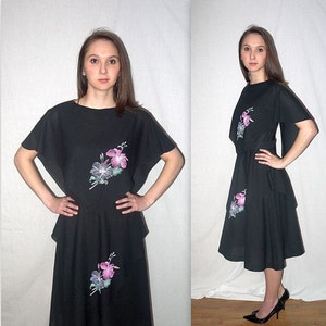 Könnte beinhalten: Schwarzes Kleid mit kurzen Ärmeln und passendem Rock. Das Kleid hat ein Blumendesign in Rosa, Lila und Weiß. Das Model trägt schwarze Absätze. Das Kleid hat einen runden Ausschnitt und eine taillierte Taille.