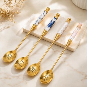 Puede incluir: Cuatro cucharas de metal dorado con mangos largos y delgados que presentan inserciones de cerámica decorativas en patrones azules, blancos y rosas. Cada cuenco de cuchara está grabado con texto personalizado, incluyendo John's Coffee Spoon, William & Sophia, MAKE TODAY TEA-RRIFIC y The Eras Tour 2026.
