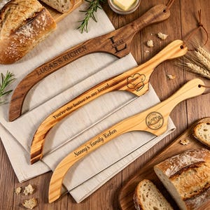 May include: Three wooden bread slicers with wire blades, each featuring unique laser-engraved text and designs. The top slicer reads LUCAS'S KITCHEN, the middle reads You're the butter to my bread with a chef hat, and the bottom reads Nanny's Family Kichen.