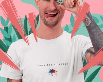 Puede incluir: Una camiseta blanca de manga corta con el texto negro "Love has no shape" impreso en el pecho sobre un pequeño gráfico colorido de salpicaduras de pintura. La camiseta está hecha de tela lisa y tiene un cuello redondo estándar.